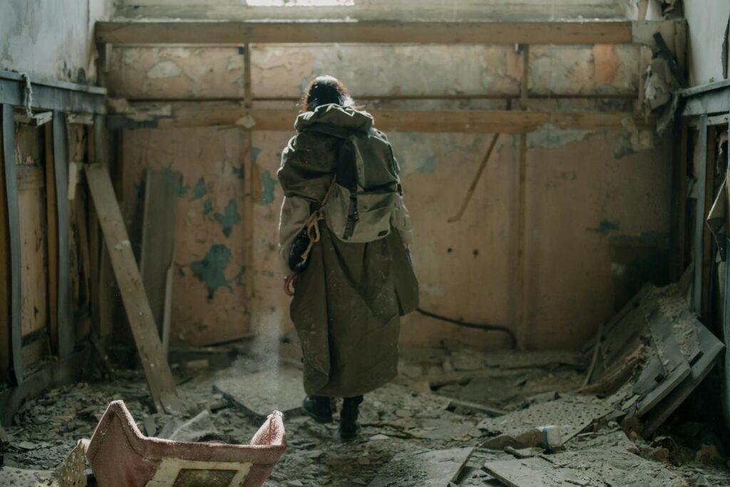 A lone figure explores an abandoned building, covered in debris and decay.